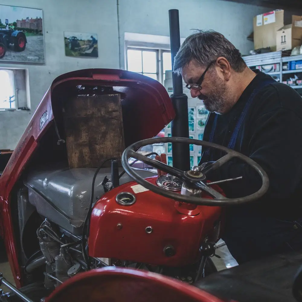 En mand kigger ned i en traktors motorrum